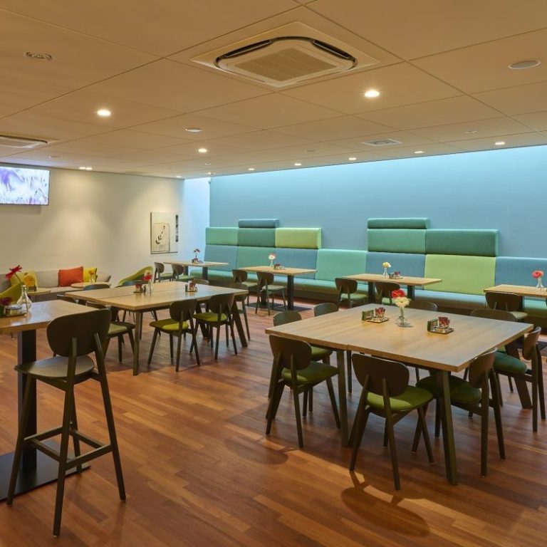 Moderne koffieruimte met houten vloeren, tafels, stoelen en zachte groene en blauwe wanden.