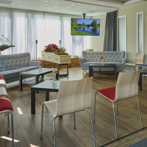 Moderne afscheidsruimte met comfortabele stoelen, tafels en een tv-scherm.