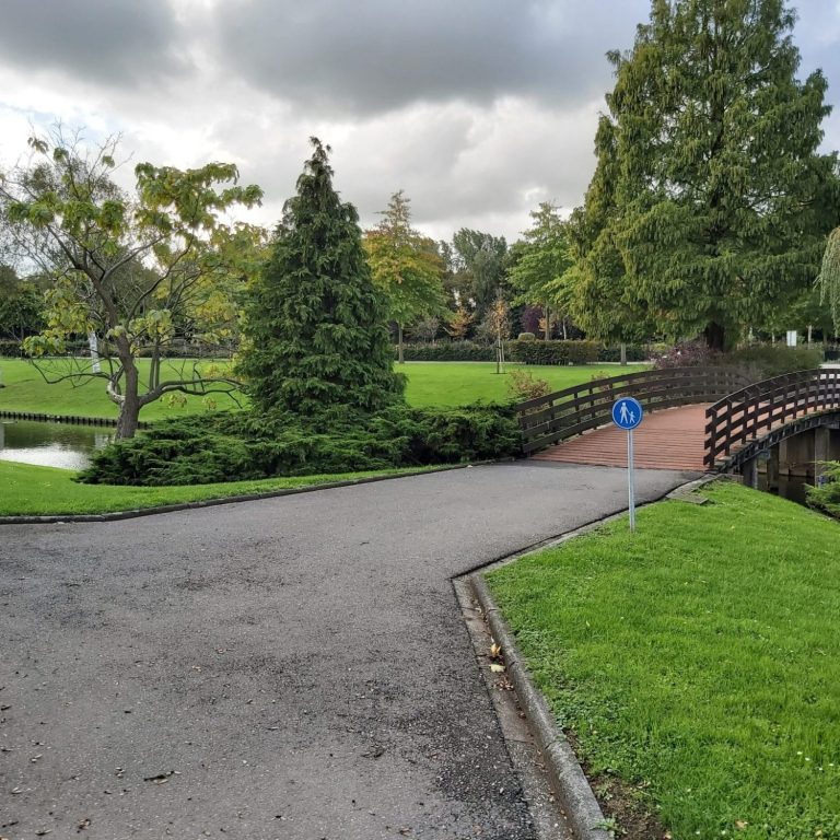 Groen park met een brug, bomen en een kronkelige weg naar het crematorium.
